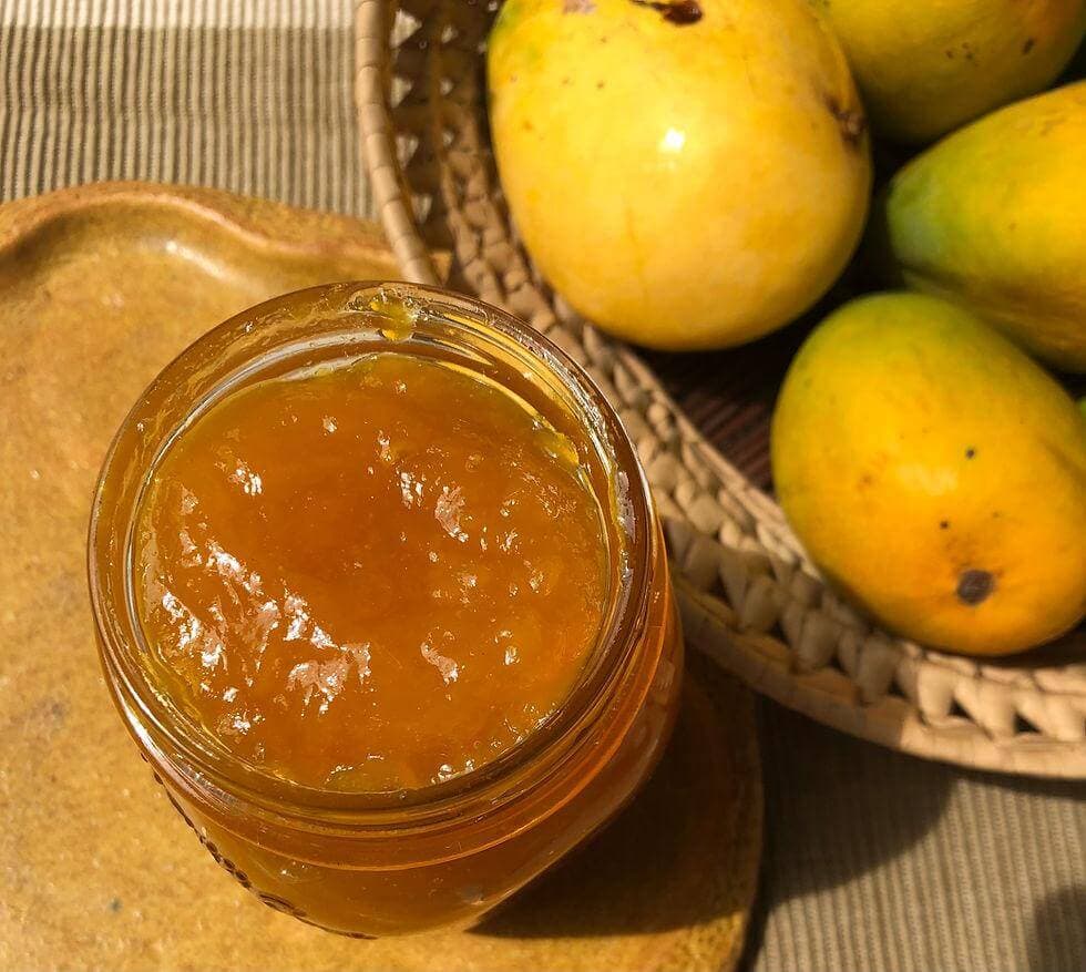 Jar of Goan mangad mango jam with fresh mangoes in a basket